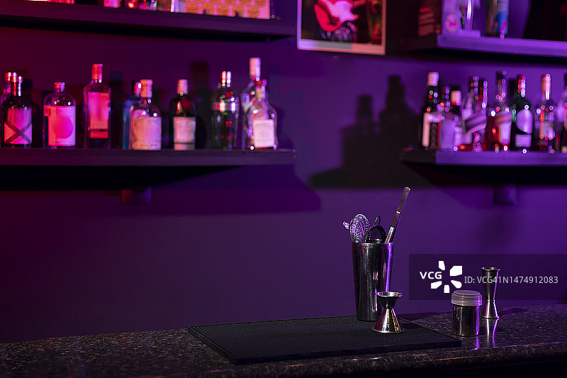 酒吧柜台，配备饮品调制工具和背景中的瓶子，并带有紫色灯光图片素材
