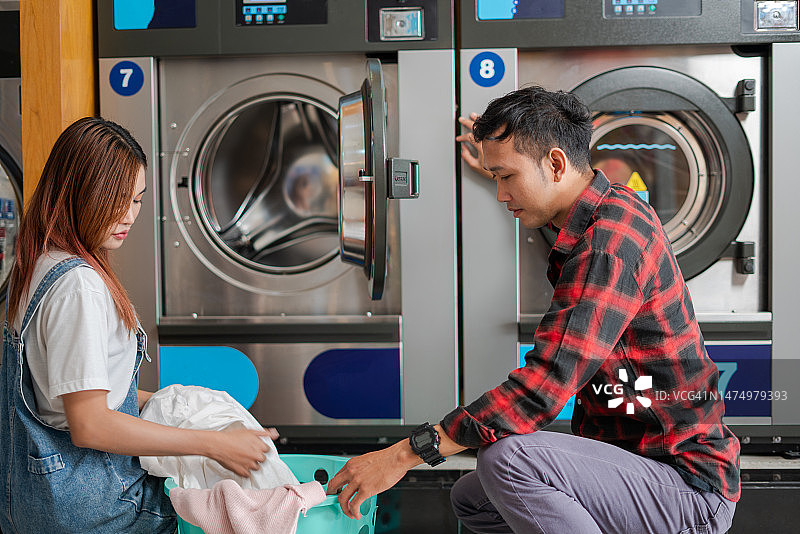 快乐的年轻夫妇在自助洗衣店一起洗衣服图片素材