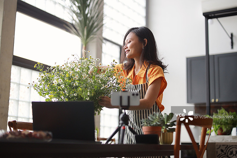 漂亮的亚洲女花商在智能手机和笔记本电脑上录制视频博客，在家中进行花束插花在线辅导。个体经营、在线学习、在线课程、小企业概念图片素材