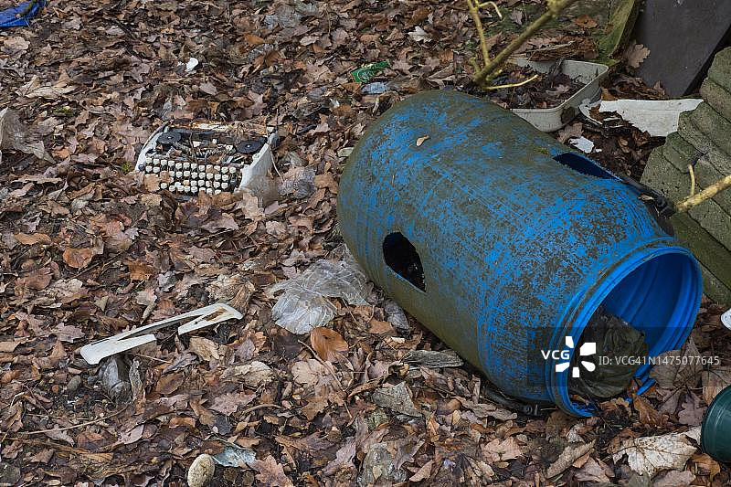 环境污染：森林地面上的破旧打字机和塑料桶图片素材
