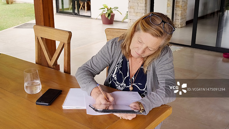 年长的女人在家使用平板电脑做笔记图片素材