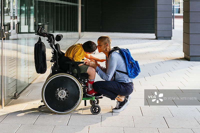 母亲蹲在市区坐在轮椅上的孩子面前图片素材