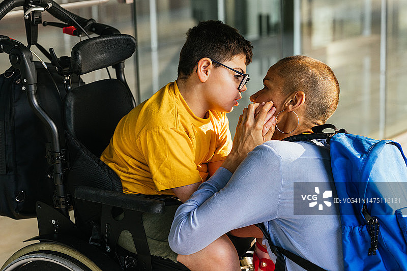 充满爱意的母亲在建筑物外直视坐在轮椅上的儿子图片素材