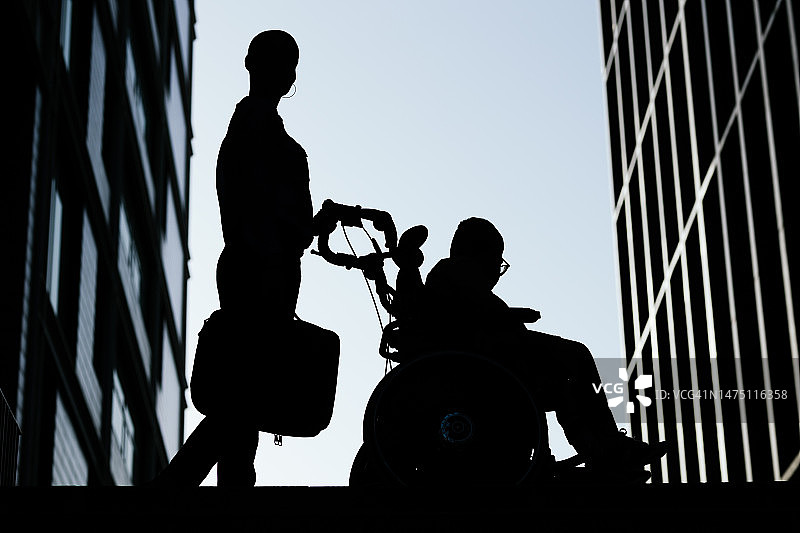 商务女性手提电脑包，与轮椅上的儿子一同行走的轮廓图片素材