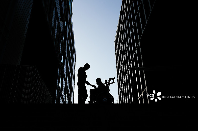坐在轮椅上的孩子在日落时牵着母亲的手的剪影图片素材