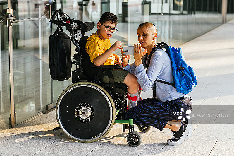 母亲向坐在轮椅上的残疾儿子展示手机视频。图片素材