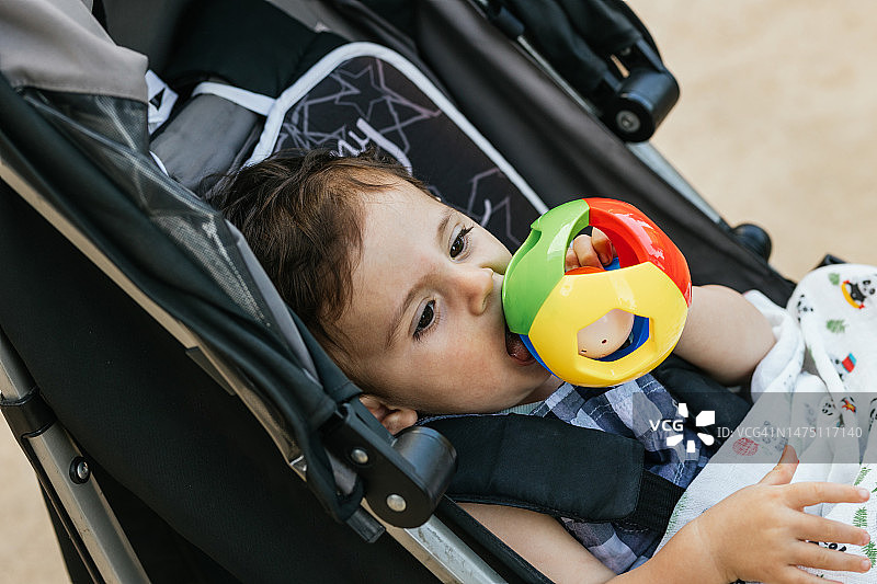 坐在婴儿车里玩玩具的漂亮黑眼睛男婴图片素材