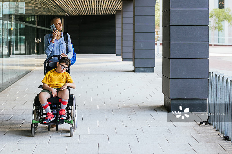 坐在轮椅上的四肢瘫痪儿童在母亲的陪伴下在城市里散步图片素材