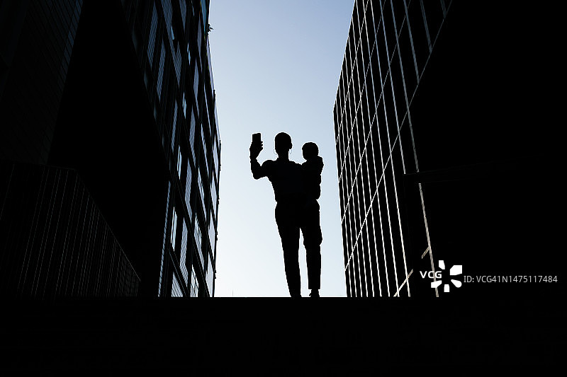 母亲抱着婴儿用手机自拍的剪影图片素材