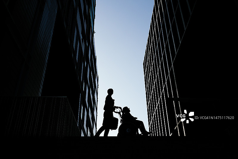 日落时分，女商人与坐轮椅的儿子回家路上的轮廓剪影图片素材