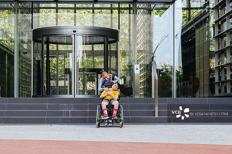 职场妈妈和坐电动车的残疾儿子在办公楼前图片素材