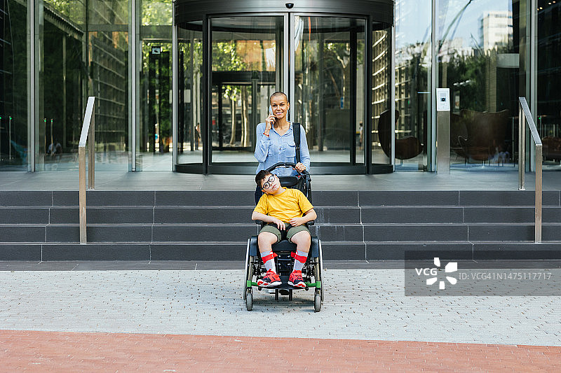 现代母亲在市中心打电话，和坐轮椅的儿子一起下班图片素材