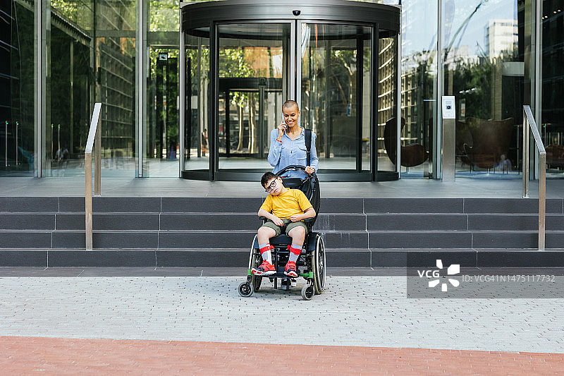女人在建筑物前打电话，儿子坐在轮椅上图片素材