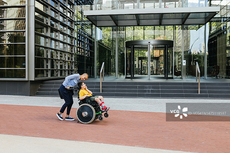 微笑地和坐在轮椅上的四肢瘫痪的儿子说话的女人图片素材