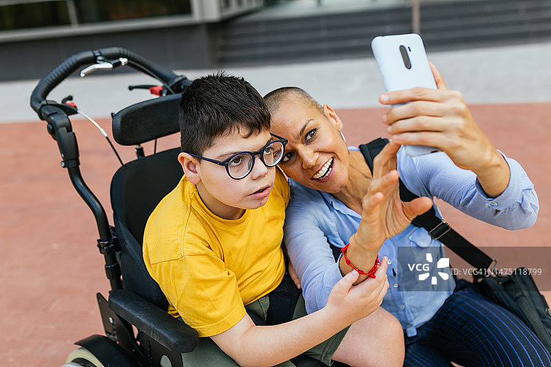 坐在轮椅上的神经多样性儿童和使用手机的母亲图片素材