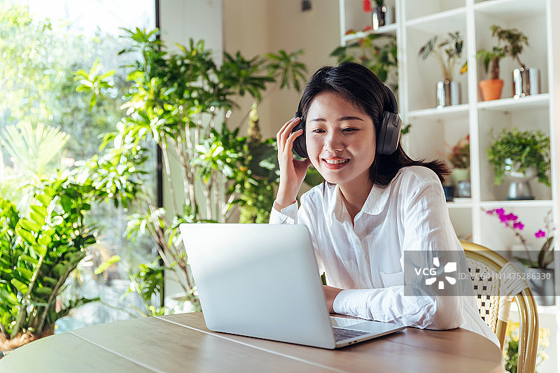 戴着耳机的亚裔女性使用笔记本电脑进行在线交流和视频聊天图片素材
