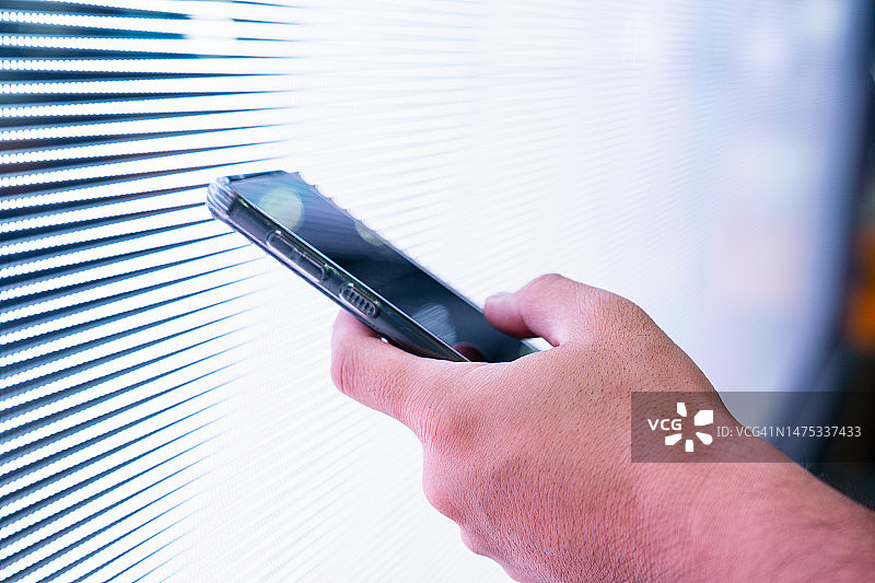 手持智能手机，城市LED数字显示屏背景，霓虹灯光。生活方式与科技图片素材