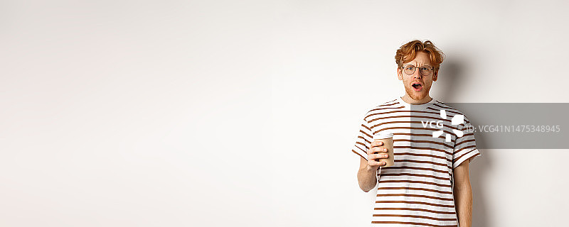 惊讶的红发男子戴着眼镜，拿着咖啡杯盯着镜头图片素材