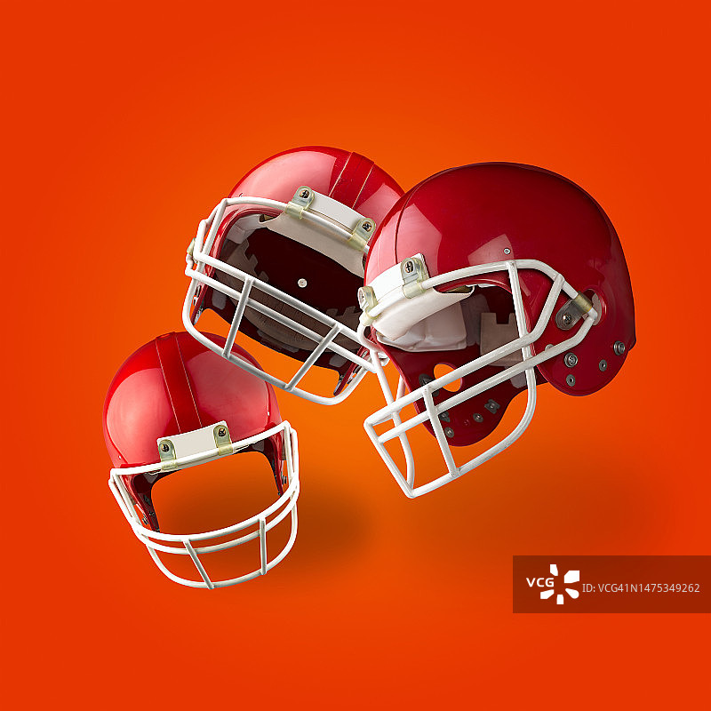 橙色渐变上的三个漂浮的红色美式橄榄球头盔图片素材