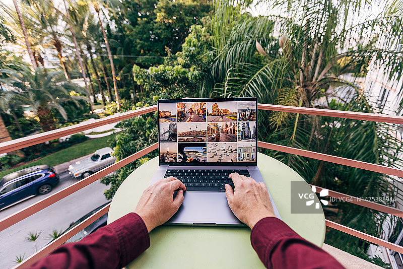 在阳光明媚的日子里，在棕榈树环绕的阳台上使用笔记本电脑的男人图片素材
