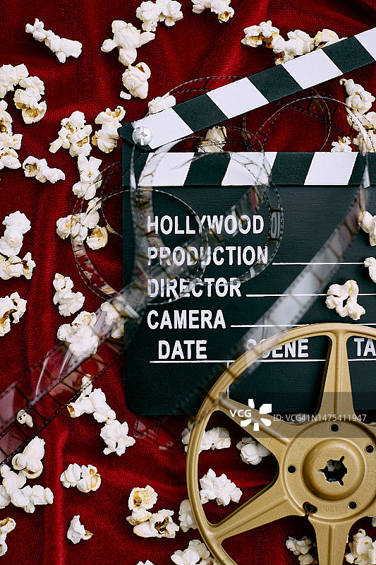 电影场记板、电影胶片、胶卷和红色缎面背景上的爆米花图片素材