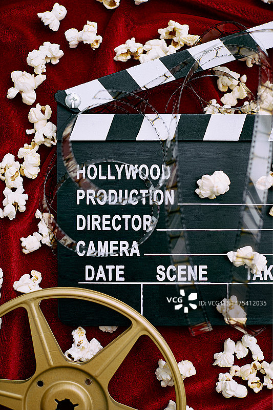 电影场记板、电影胶片、胶卷和红色缎面背景上的爆米花图片素材