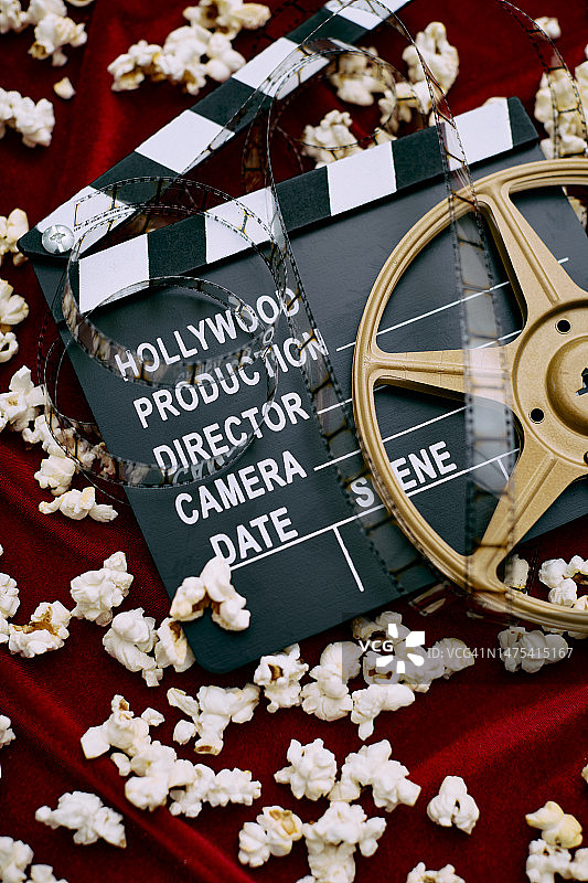 电影场记板、电影胶片、胶卷和红色缎面背景上的爆米花图片素材