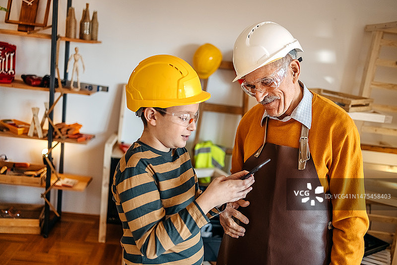 男孩用无线科技帮助爷爷在木工车间工作图片素材