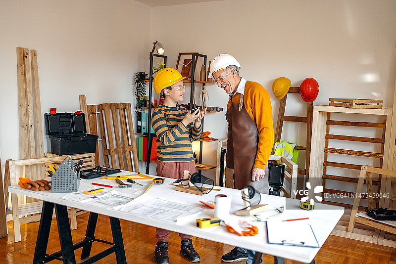 男孩用无线科技帮助爷爷在木工车间工作图片素材