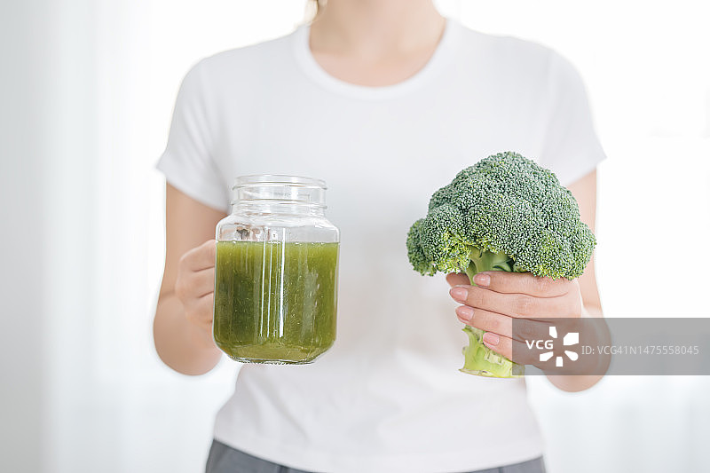 富含维生素和矿物质的纯素冰沙：一位素食女性在家中手持新鲜西兰花和西兰花冰沙，用于健康饮食的特写镜头图片素材