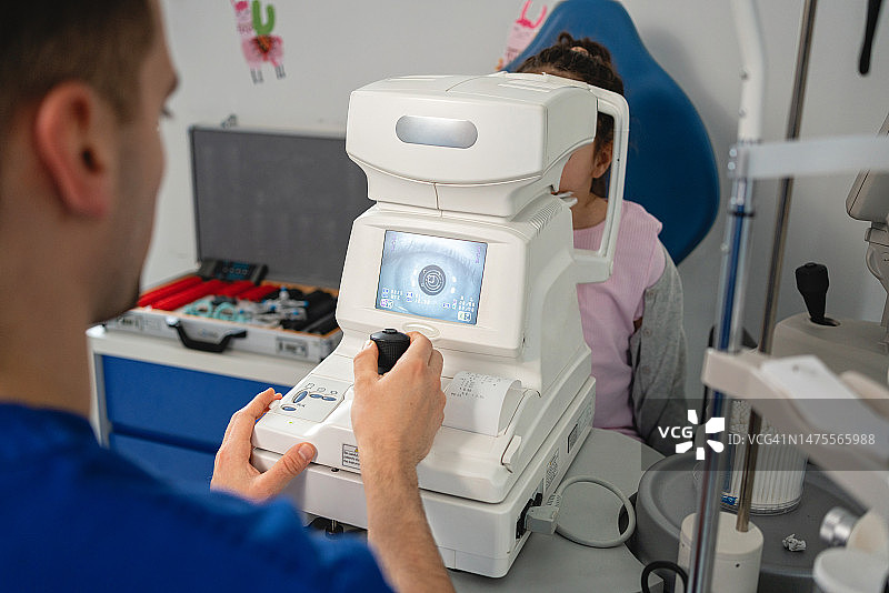 在诊所使用自动验光仪检查小女孩眼睛的男眼科医生图片素材