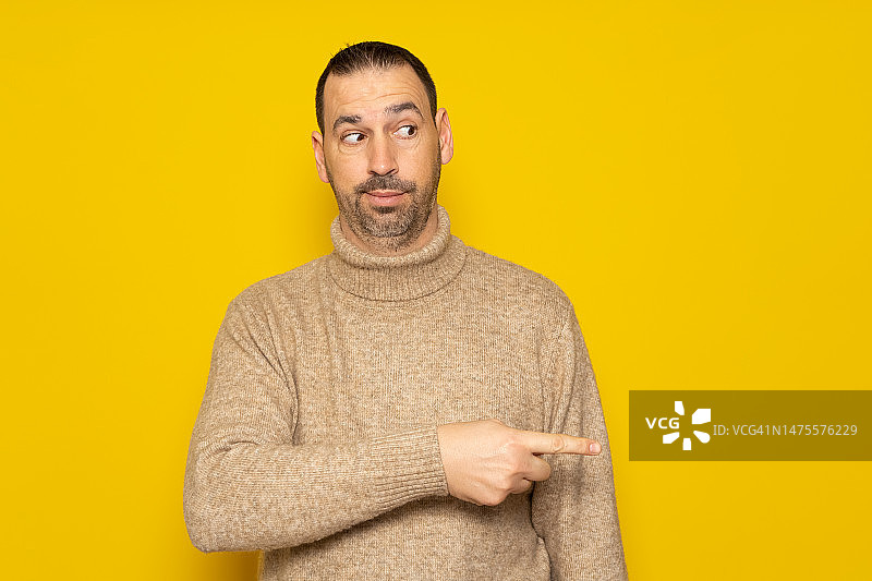 留胡须穿米色高领毛衣的拉丁裔男人指向旁边图片素材