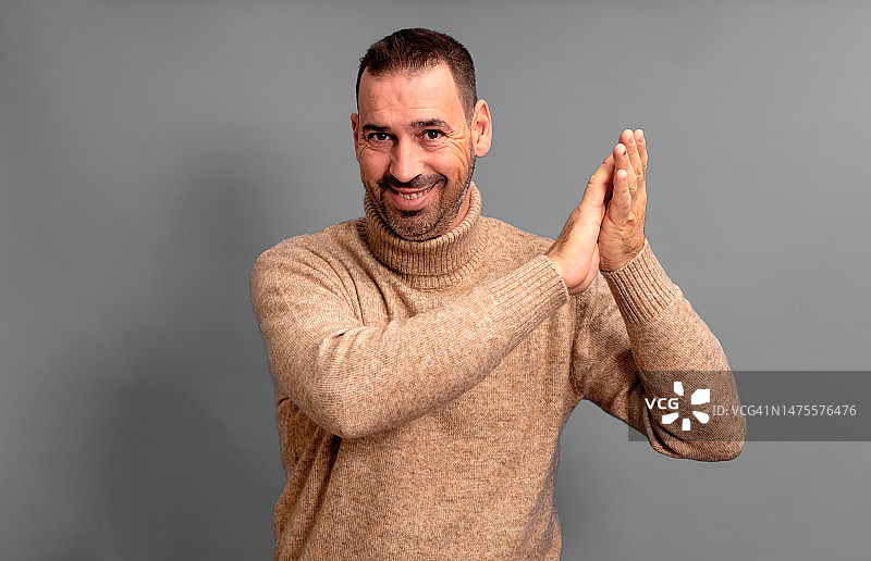 鼓掌的西班牙裔胡须男，身穿米色高领毛衣图片素材