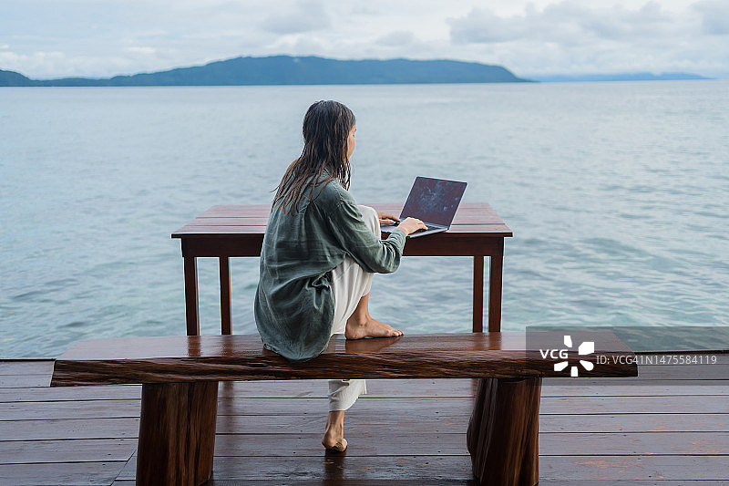 年轻女人在泻湖上的码头上远程工作图片素材
