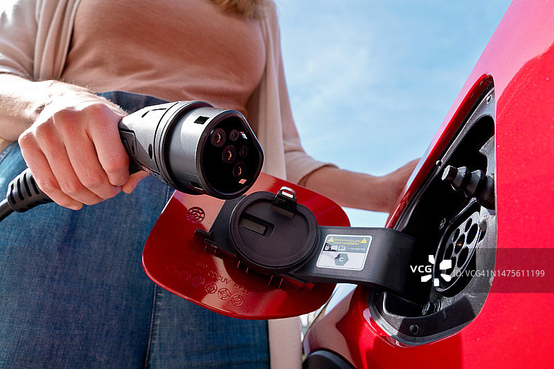 女子手持电动汽车充电器插头特写图片素材