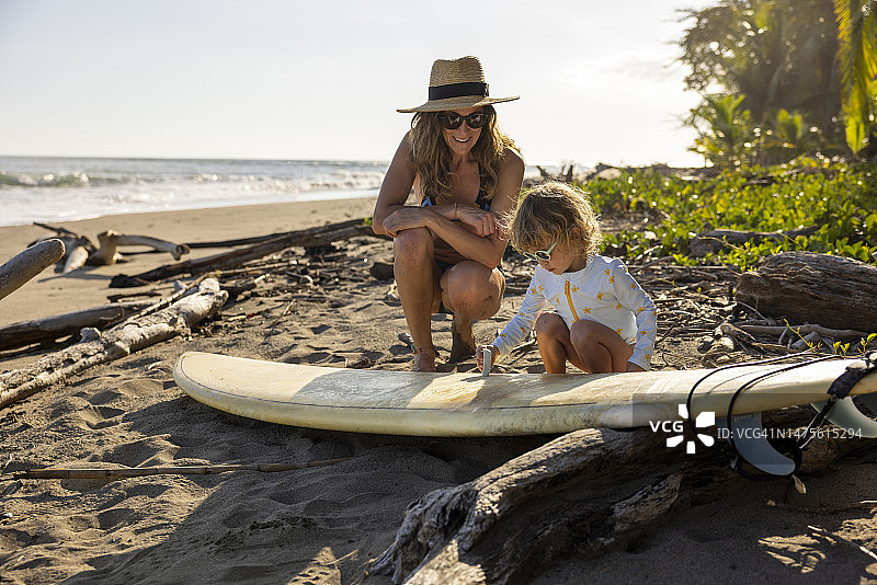 年轻女孩向母亲学习如何给冲浪板打蜡图片素材