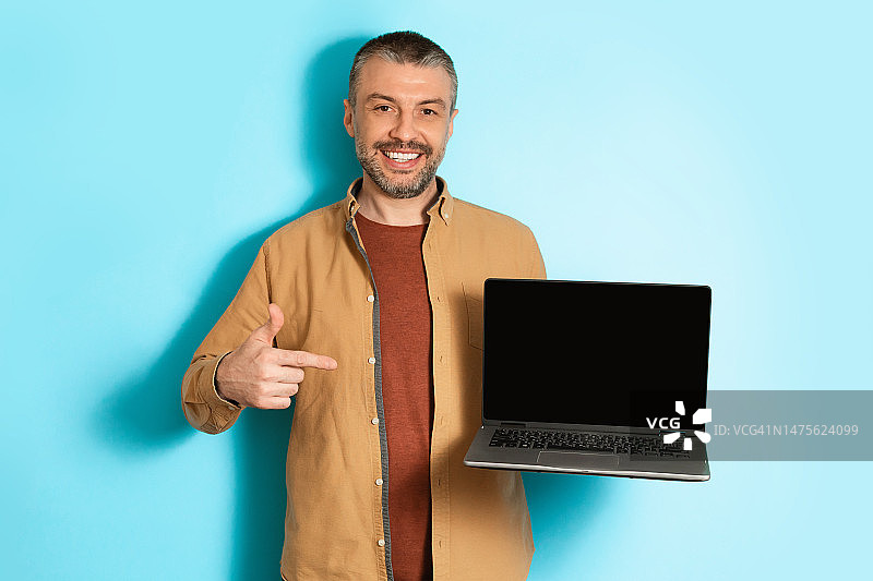 男人拿着笔记本电脑，指向蓝色背景上的空白屏幕图片素材