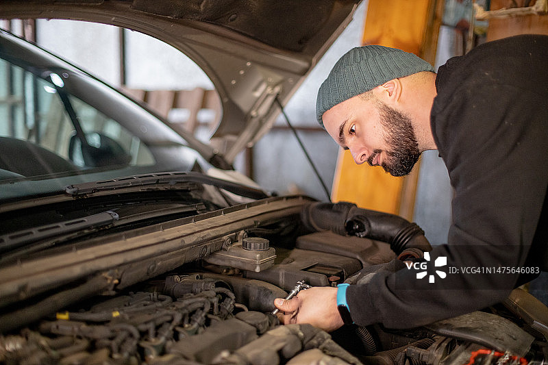在家中车库维修汽车的年轻男人，他正在拧开一些螺丝图片素材