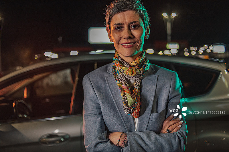 一位商务女性在停车场站在她的车旁的傍晚照片图片素材