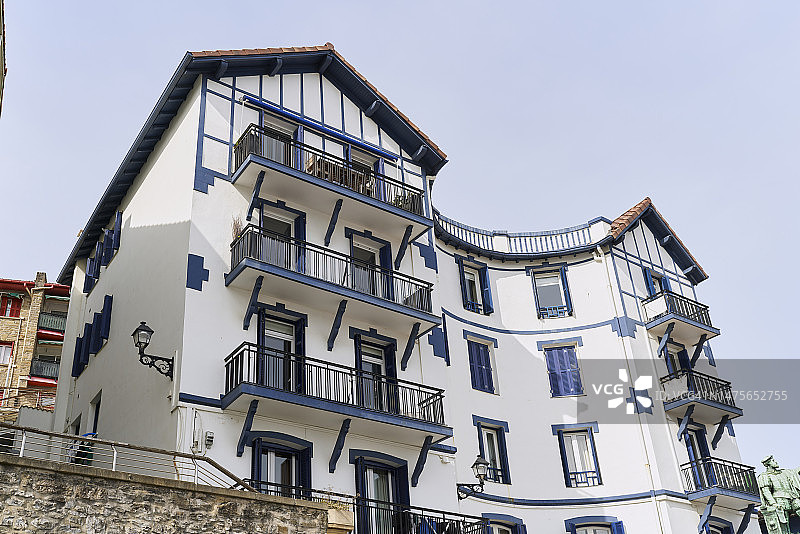 一栋大型建筑，有多个阳台和窗户，漆成白色，带有蓝色细节，窗户带有蓝色百叶窗，一些灯笼和瓷砖屋顶图片素材