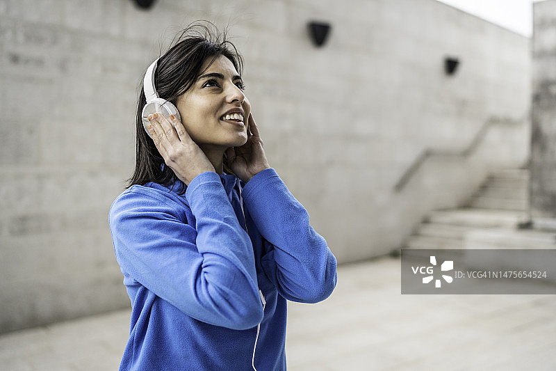 在城市背景下听音乐的年轻快乐的运动型女人图片素材
