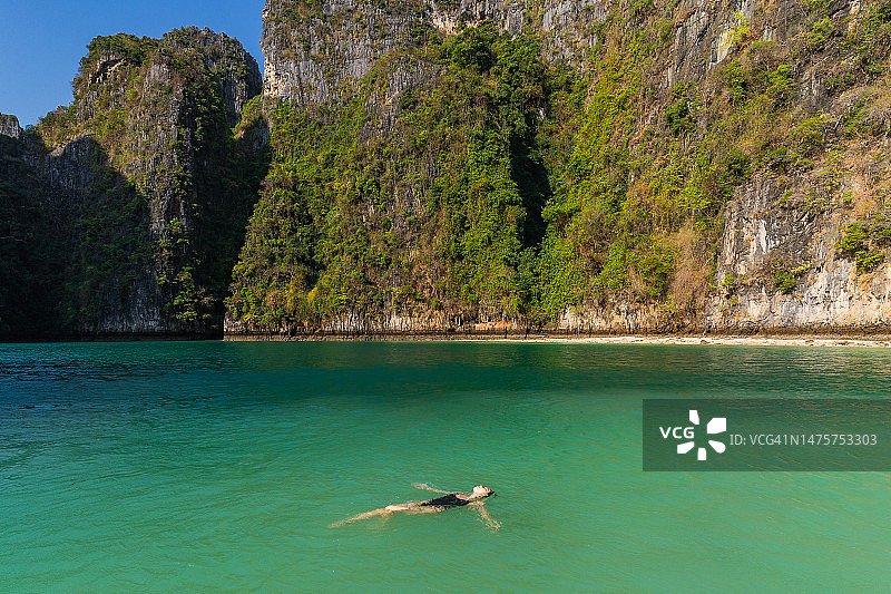 在泰国甲米府皮皮岛，一位比基尼穿着者漂浮在绿色的海水中，背景是山脉图片素材