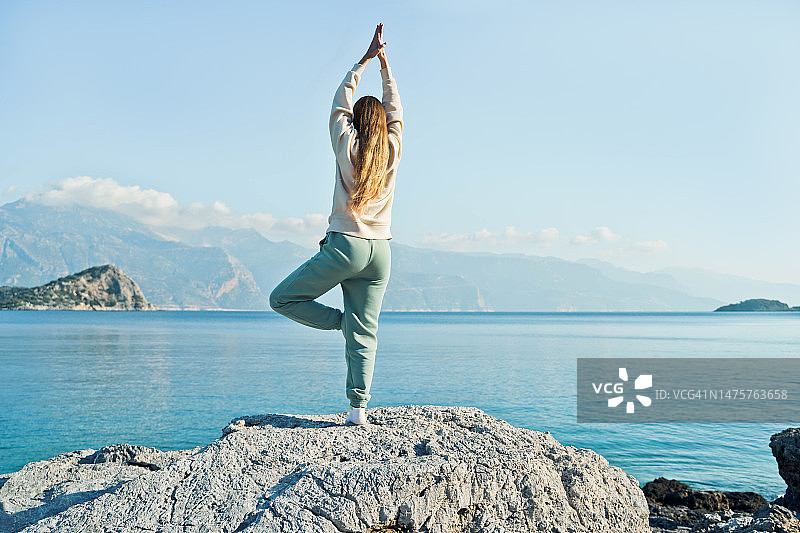 年轻女子在石头上练习瑜伽，美丽的海景背景。全身照。图片素材