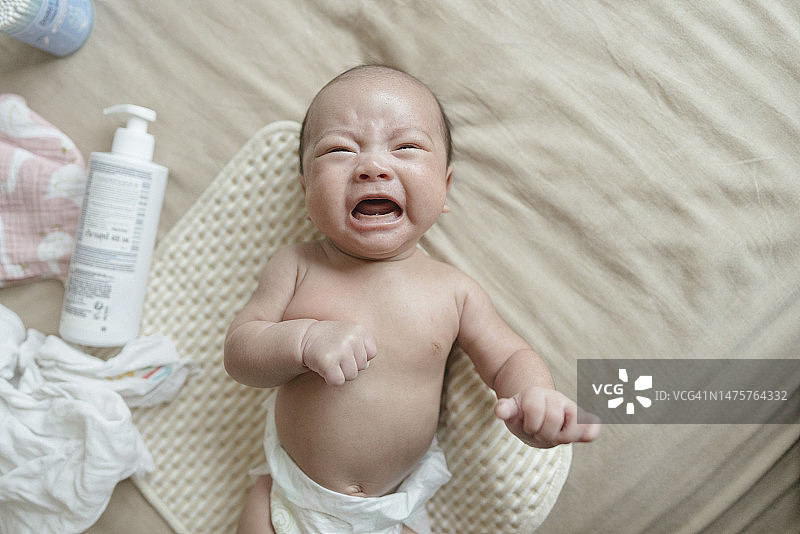 新生亚洲宝宝躺在床上哭泣，妈妈正在换尿布图片素材