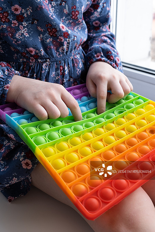 按压式指尖玩具。小女孩玩彩虹的颜色。儿童手中的抗压感官玩具。图片素材