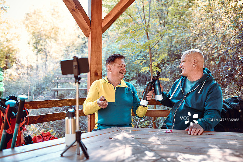 微笑的老年男性登山者在凉亭里喝水休息时自拍图片素材