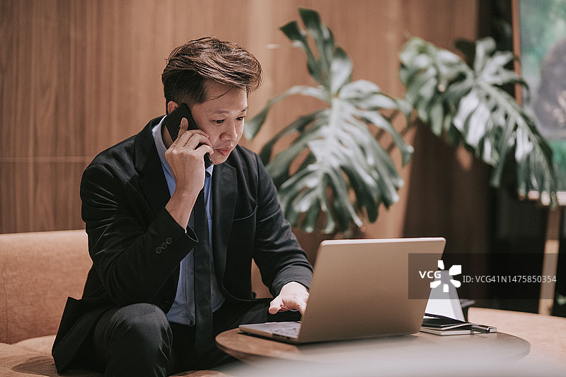 在机场休息室用笔记本电脑打电话的亚洲商人图片素材