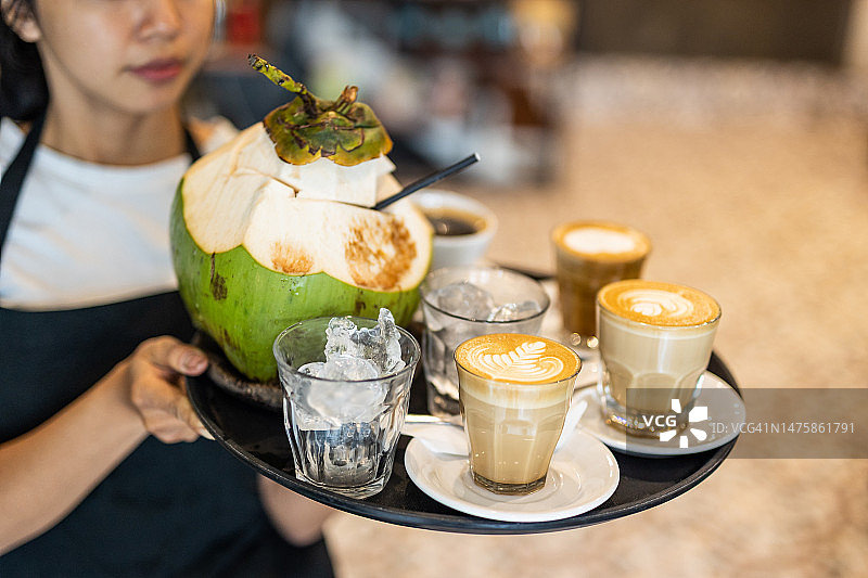 在巴厘岛餐厅工作的年轻漂亮女服务员为客人提供卡布奇诺或椰奶饮品图片素材