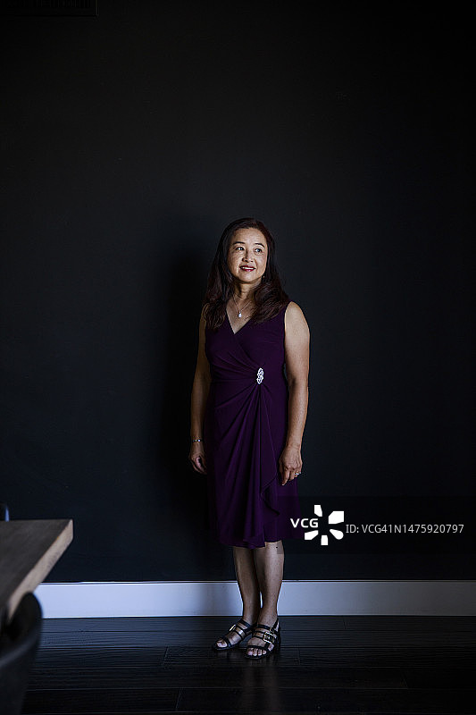 笑容满面的中年妇女靠在黑墙边，目光移开图片素材