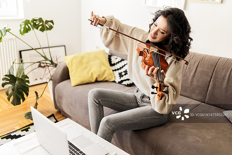 年轻小提琴手在客厅使用笔记本电脑在家练习图片素材